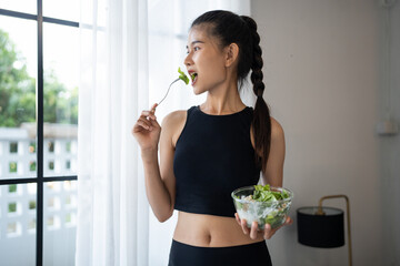 Naklejka premium Fitness asian woman eating healthy salad after workout. Smiling Beautiful asian young female eating healthy food after exercise training in yoga studio healthy lifestyle
