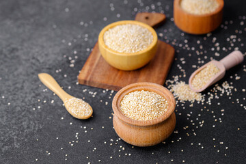 Quinoa seeds in multiple wooden bowls and spoons on dark background