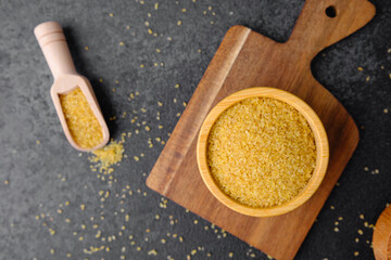 Cracked wheat groats in wooden bowl on black background. Healthy raw cereal grains.