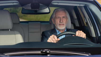 Un homme senior conduit une voiture en plein jour, concentr&eacute; sur la route