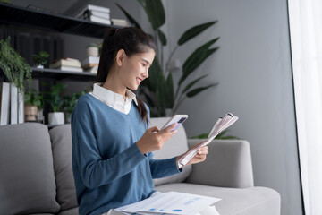 Asian woman holding paper document calculating money savings paying bills in mobile application...