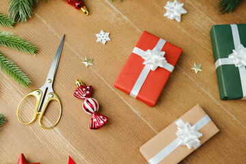 Wrapping gifts with red and green presents, scissors, candy ornament, and pine branches on wood