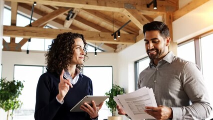Real estate agent points to wooden beam ceiling while showing modern home interior to smiling male client holding paperwork