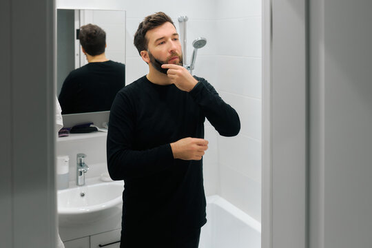 Man grooming in bathroom mirror during morning routine while preparing for the day ahead