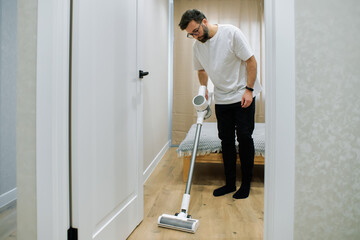Man using a vacuum cleaner while cleaning a wooden floor in a modern home interior during day time © makedonski2015