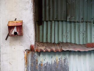 A red mail box, white wall and rusty weathered zinc with some incent sticks.