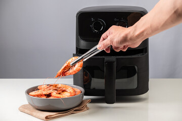 Man Placing Shrimp from Modern Black Air Fryer.
