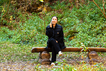 Woman freelancer wear linen dress, sitting on chair in green house, resting, using smartphone and drinking tea from a mug in harmony with the plants around. Home garden, freelance. 