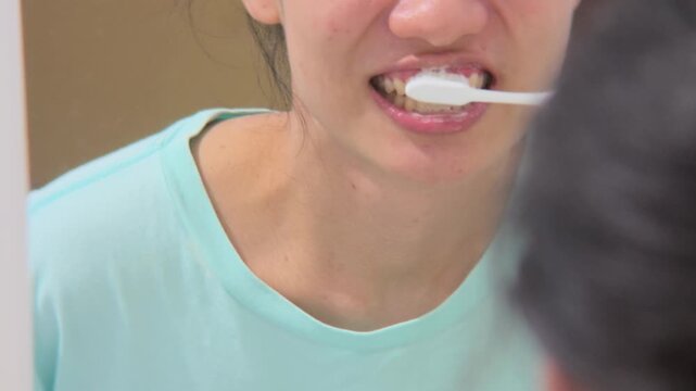Slow motion Woman brushing her teeth getting ready in the morning doing hygiene routine looking in mirror of home bathroom using toothbrush in for clean dental oral care.
