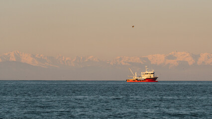 a fishing trawler sails on the sea against the backdrop of mountains