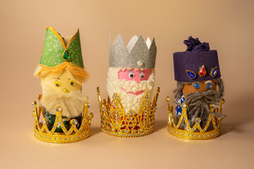 Three handmade Three Kings figurines placed inside of crowns are displayed on a beige background, symbolizing Epiphany celebration on January 6.