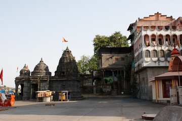 View of an ancient stone temple complex in Nashik with carved shikhara towers, open courtyard, and old surrounding buildings under clear daylight.
