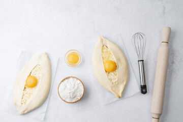 Uncooked khachapuri with egg yolk and whisk on white background