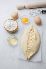 Unbaked khachapuri with cheese on parchment and baking ingredients