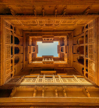 Warm sunlit view of Patwa Haveli&rsquo;s carved sandstone courtyard in Jaisalmer, captured from below with a perfect architectural frame toward the open sky.