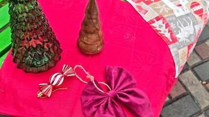 Glass Christmas tree, wooden tree figurine, striped candy ornament and burgundy bow lie on a red...