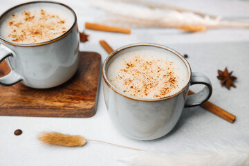 Warm milky drinks topped with cinnamon in ceramic mugs with spices and soft dried grass