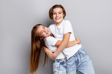 Happy children hugging and smiling in studio, playful friends enjoying fun moment together in casual white t-shirts, isolated on clean grey background