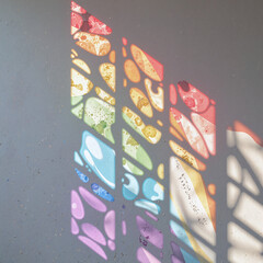 Stained glass pieces forming a rainbow pattern, sunlight refracting colorful rays onto a white wall,Through refracted light, the message of love and diversity shines brightly.