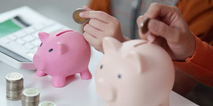 Saving Money. Child placing coins into piggy banks with parental guidance. - Powered by Adobe