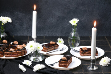 Chocolate cakes served with white flowers and lit candles on dark background