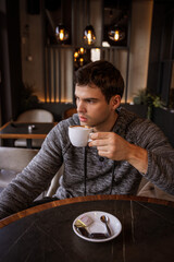 Young man sits alone in a café drinking a cappuccino