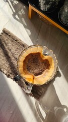 An aerial view shows freshly brewed coffee dripping into a glass dripper placed on a light brown towel, with morning sunlight casting beautiful shadows on the light-colored tile floor.