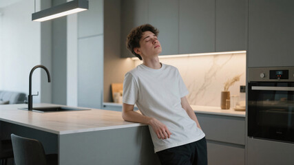 Bright contemporary kitchen interior with soft neutral finishes, showing a young adult leaning on the island, pausing to breathe while recovering from mild post-viral fatigue in a polished wellness-fo