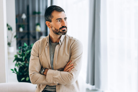 Middle aged bearded man with crossed arms looking to the right with pensive expression