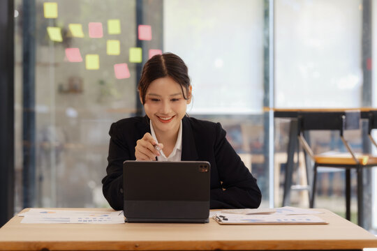 An Asian businesswoman smiling and working on a digital tablet at an office desk.