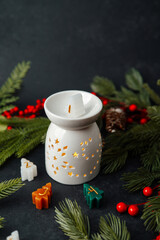 Ceramic diffuser with lit candle and festive mini tree shaped candles surrounded by evergreen branches.