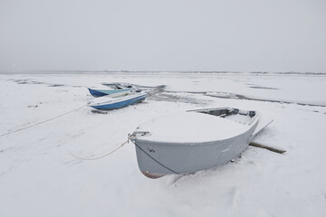 Motorboats in winter under the snow on the river bank in the fog