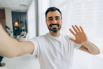 Smiling middle aged adult man waving hand during video call