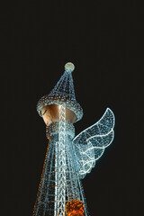 Obraz premium Giant glowing angel figure with wings at night, illuminated by white and blue lights.