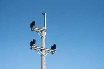 An electric pole with insulators and wires set against a clear blue sky on a bright day