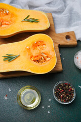 Halved butternut squash with rosemary, oil, salt, and pepper on a cutting board.