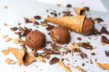 Chocolate ice cream scoops with waffle cones and chocolate chunks on light background