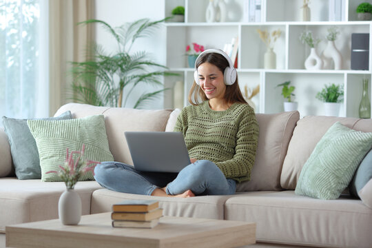 Happy woman in green wearing headphone using laptop at home
