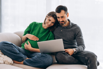 Pregnant couple watching laptop together on sofa at home