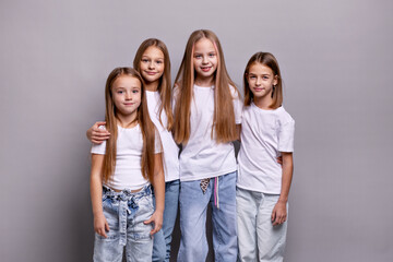 Group of beautiful young preteen girls posing in studio against gray background. Fashion portrait of stylish child models in white t-shirts and denim jeans with confident expressions