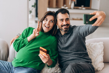 Expecting couple taking happy selfie on sofa at home