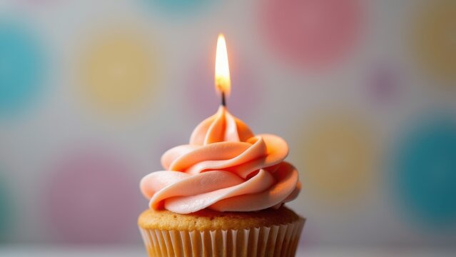 Single pastel rainbow cupcake with swirled buttercream frosting and lit golden candle on soft pink mint blurred background with copyspace, concept of birthday wishes, bakeries, greeting cards