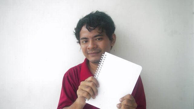 Sixteen frames show an asian man in a red shirt holding a spiral notebook. He is smiling and pointing at the notebook, and giving a thumbs up. Shot against a white wall background.