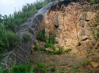 Mountain cliff with vegetation and metal mesh protection.