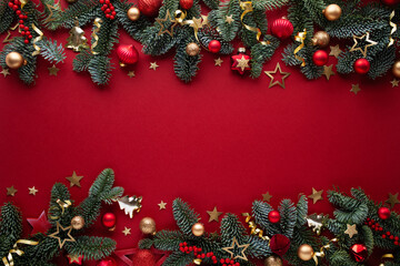 Obraz premium Bright and festive Christmas border with composition of fir branches, red berries and golden baubles on red background with empty space for your design.