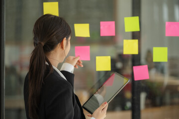 Confident businesswoman planning while looking at adhesive notes stuck on a glass wall.