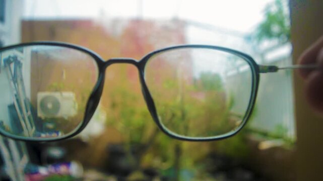 Footage showcases glasses with clear, blurry, and foggy lenses, reflecting an outdoor scene with plants and a building. Demonstrates vision clarity, impairment, and lens technology concept.