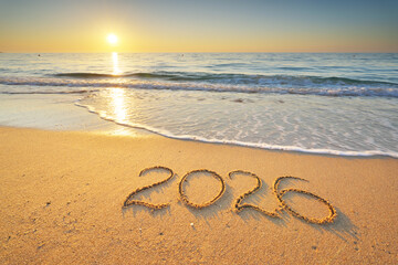 Naklejka premium 2026 text symbol of new year on the sea sand beach shore during sunset.