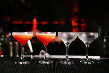 Row of finished cocktails and prepared glasses with salt rims on a dark bar counter ready for serving