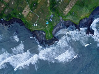 Top-down of waves crashing on rocky coastline beside rice fields